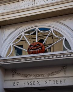 A carved, grinning pumpkin sits in the arched window above the entrance to 217 Essex Street in Salem, Massachusetts, reflecting the town's Halloween spirit.
