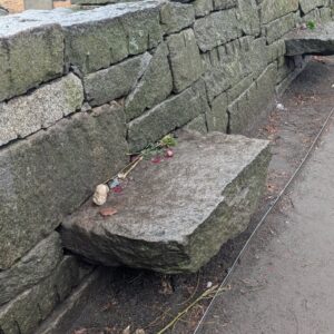 A simple stone bench at the Salem Witch Trials Memorial, adorned with flowers and small tokens left by visitors, surrounded by a stone wall.