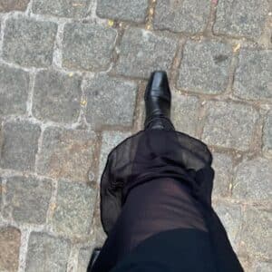 A person wearing a sheer black skirt and black pointed boots walking on a cobblestone street in Salem, Massachusetts, showcasing a fashionable and moody look.