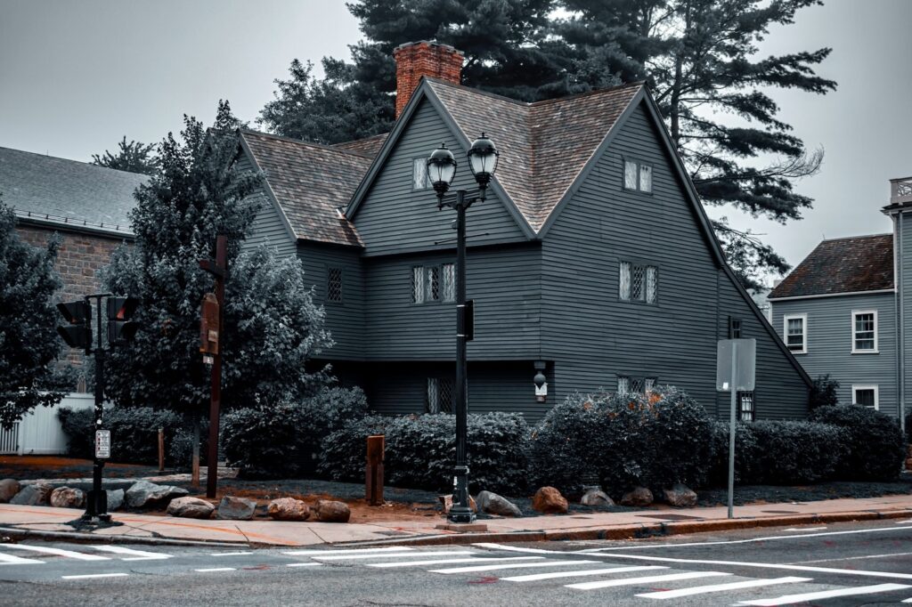 A moody view of the Salem Witch House in Salem, Massachusetts, with dark wooden architecture framed by trees and a cloudy sky, evoking its deep historical significance.