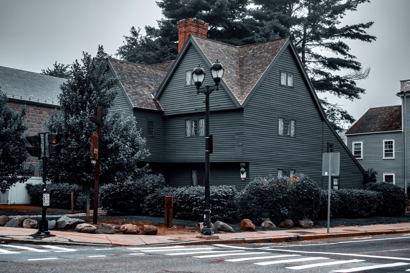 A moody view of the Salem Witch House in Salem, Massachusetts, with dark wooden architecture framed by trees and a cloudy sky, evoking its deep historical significance.