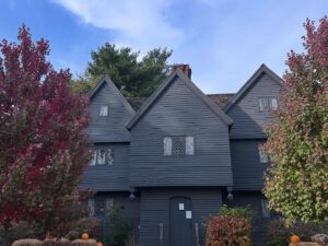 The Witch House in Salem, Massachusetts, surrounded by vibrant autumn trees with red and green foliage against a blue sky.