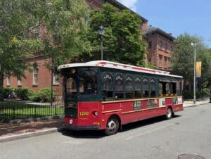 The Salem Trolley in Salem, Massachusetts, parked on a tree-lined street near historic red brick buildings on a sunny day.