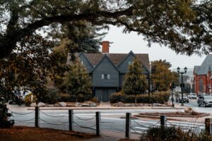 The historic Salem Witch House surrounded by trees and autumn leaves, with a street view of the surrounding area in Salem, Massachusetts.