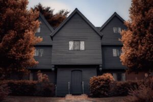 The Witch House in Salem, Massachusetts, surrounded by vivid autumn-colored trees, its dark wooden exterior adding a dramatic contrast under the soft, overcast sky.