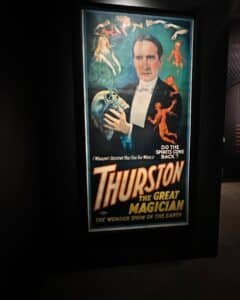 A vintage magic show poster featuring "Thurston the Great Magician" displayed at the Peabody Essex Museum in Salem, Massachusetts. The poster depicts Thurston holding a skull, surrounded by ghostly figures and red devils.