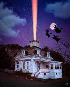 The Hocus Pocus house in Salem, Massachusetts, illuminated by a magical beam of light shooting into the night sky, with three silhouetted witches flying against a backdrop of a full moon and starry sky.