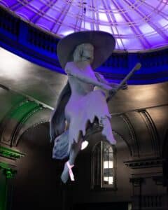 A striking witch statue suspended under a glowing purple and blue dome at Blackcraft in Salem, Massachusetts.